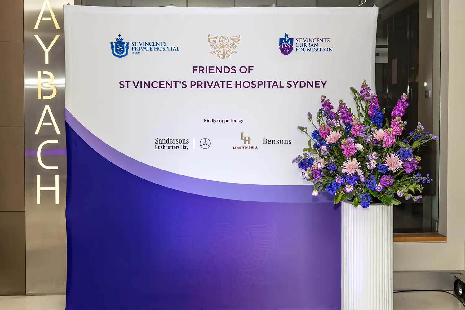 Photos of the Media wall of Friends of St Vincent's Private Hospital Sydney, Currans Foundation, with a vase of flowers in front.